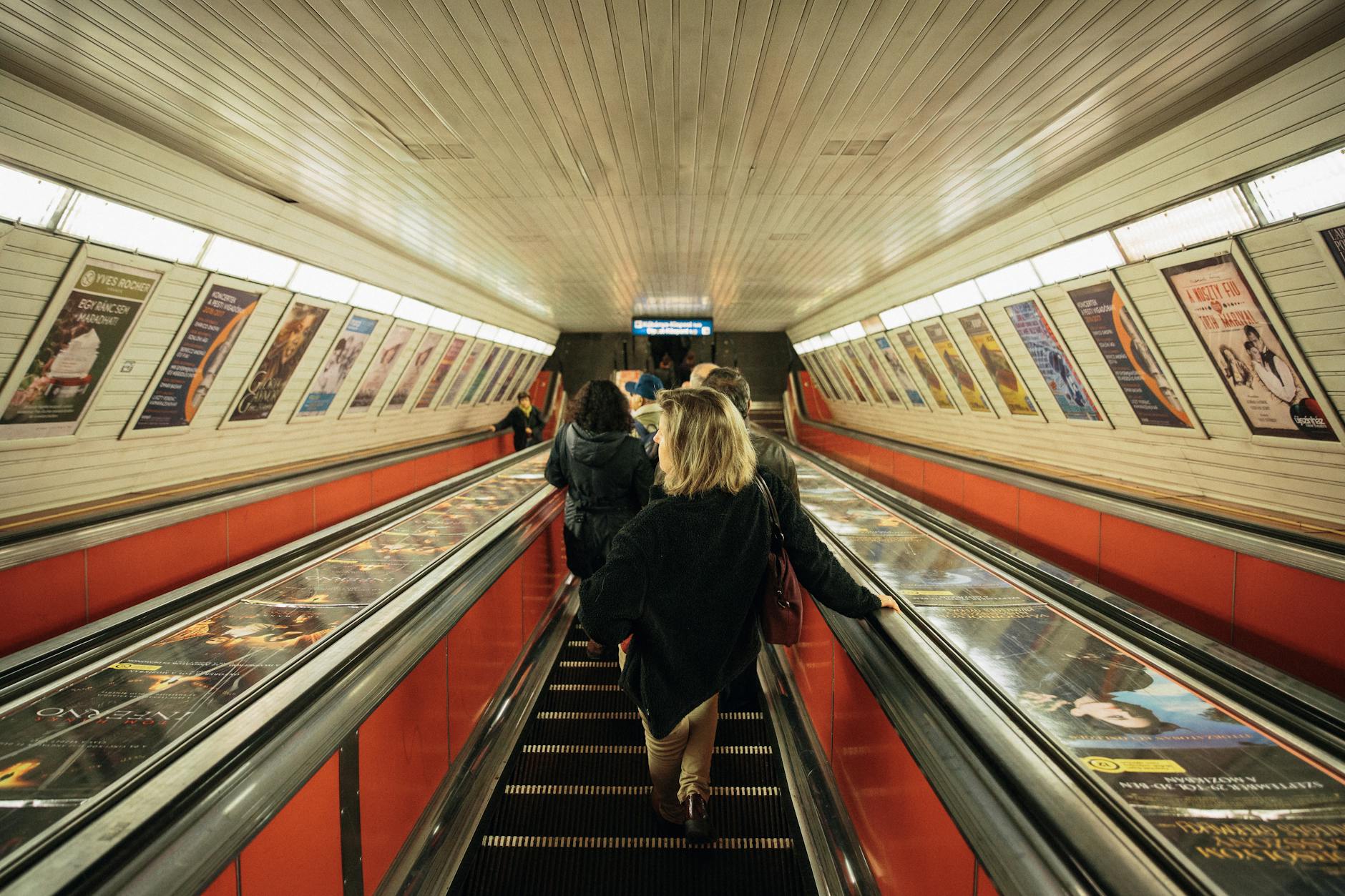 Commuters on an escalator in a Budapest metro station, Hungary, featuring vibrant posters.