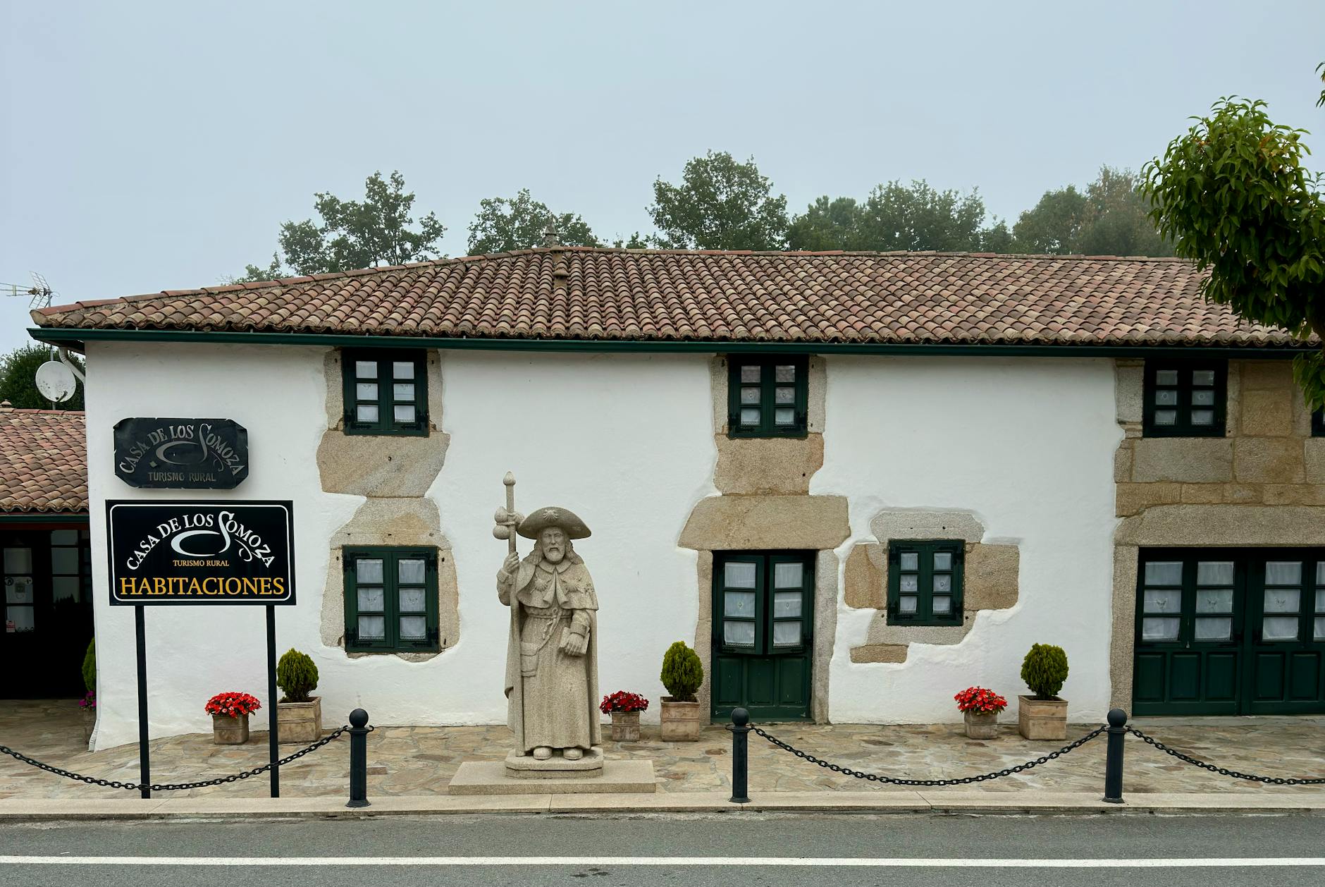 Cozy rural house with stone facade and historic statue in a quaint setting.