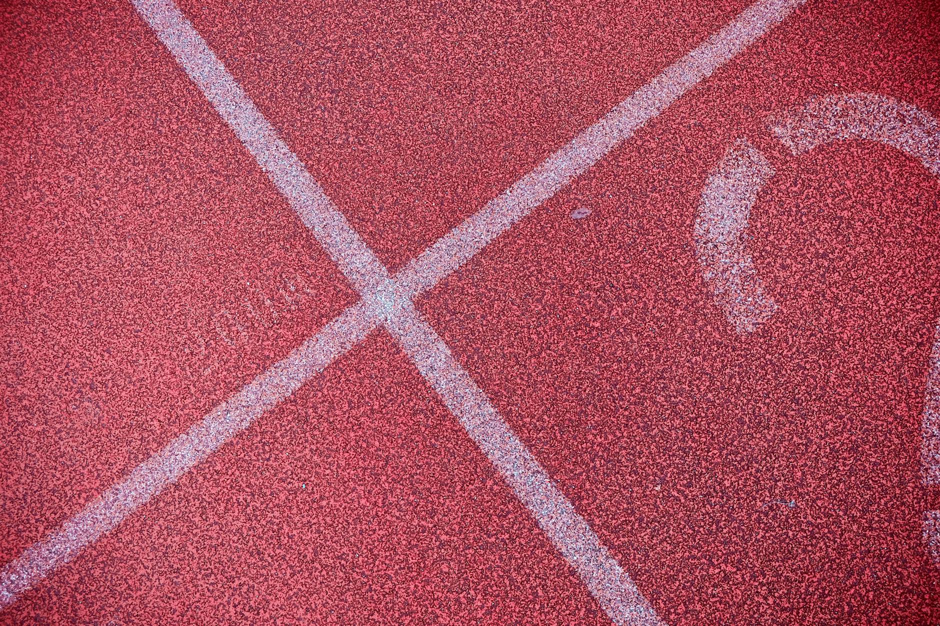 Detailed shot of a red running track showing white lane markings for athletics.