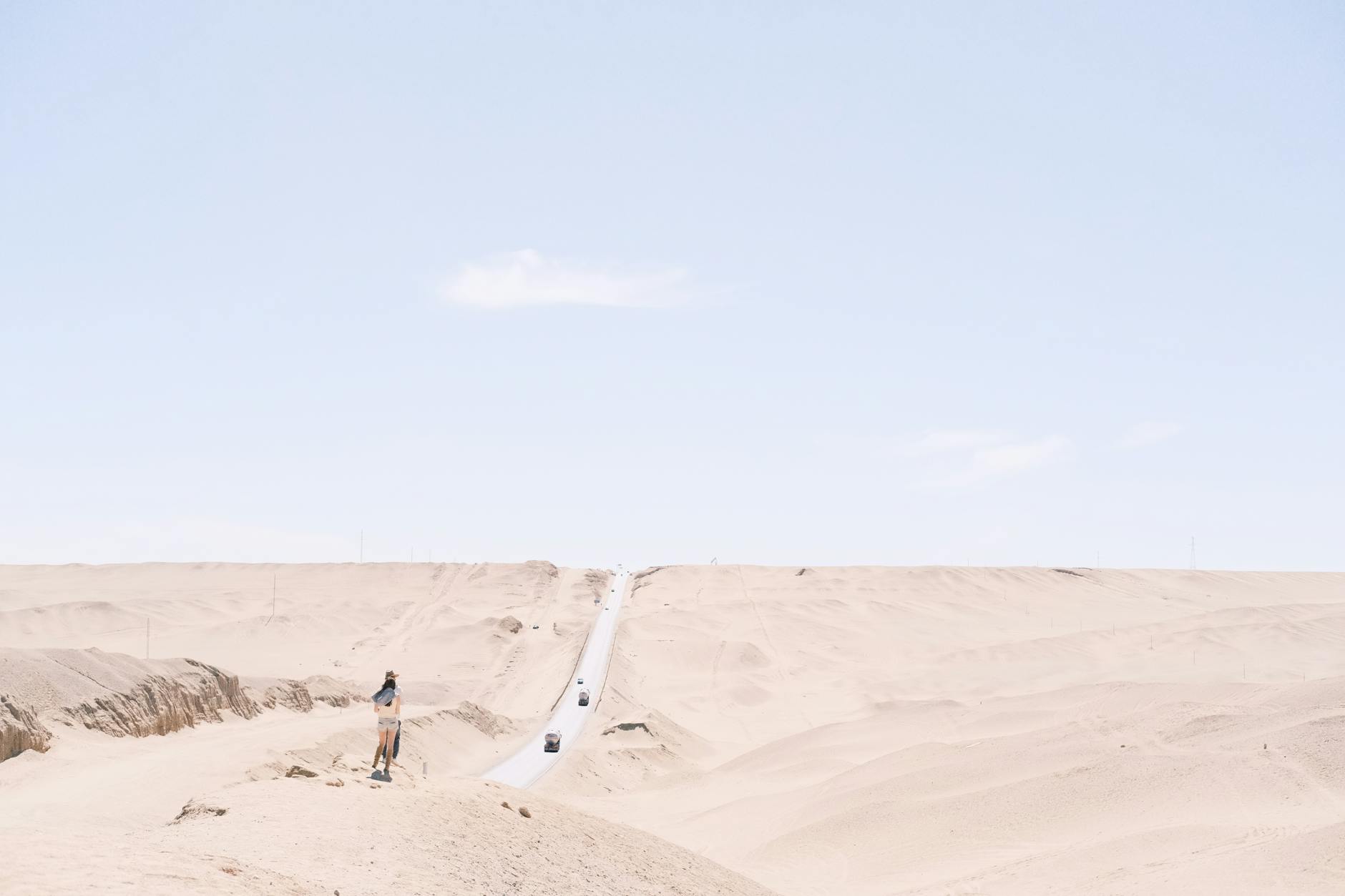 Expansive desert landscape with a solitary road leading towards the horizon under a bright sky.