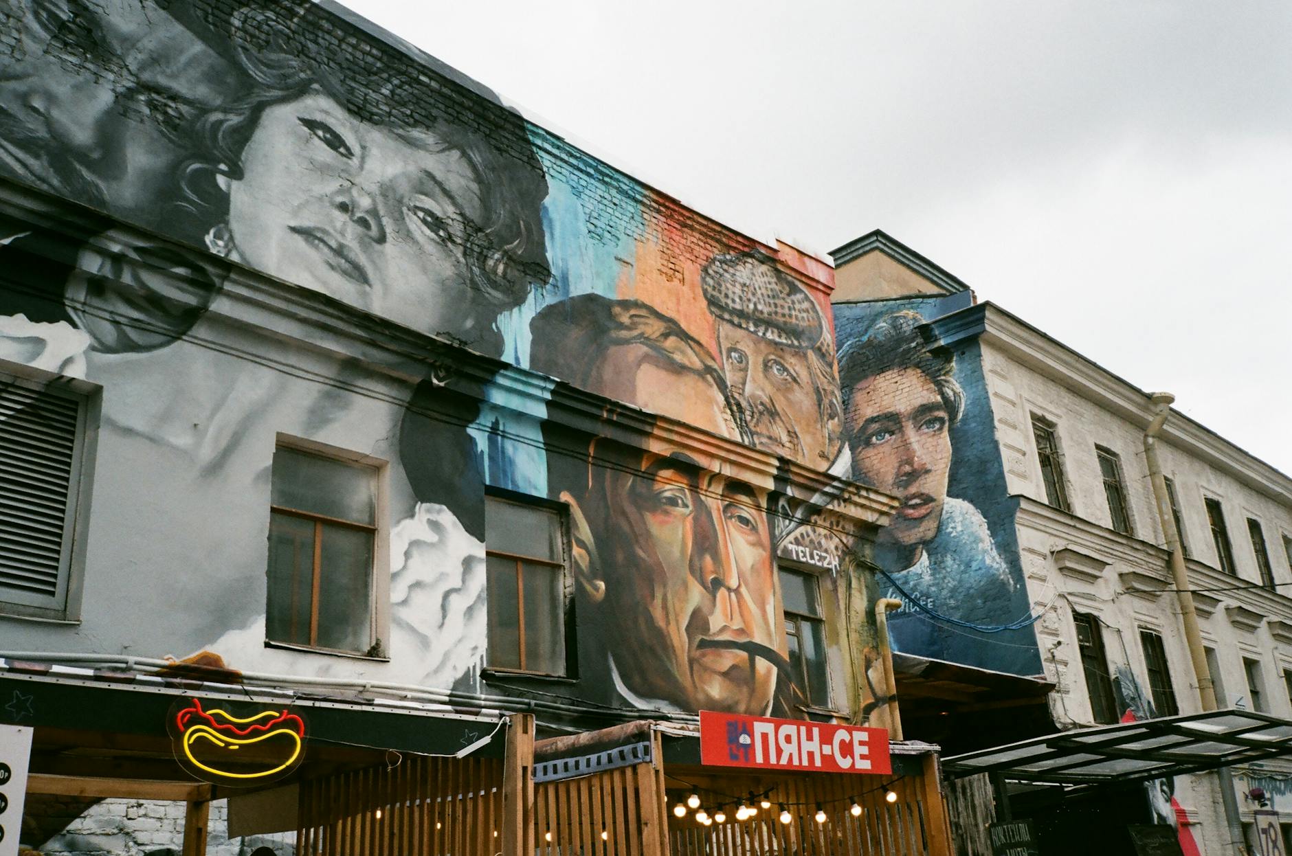 Street art: o que levar para um passeio longo sem derreter ao sol 9 Facade of aged building with cafe and creative graffiti with famous people on wall in city street in daylight against gray sky