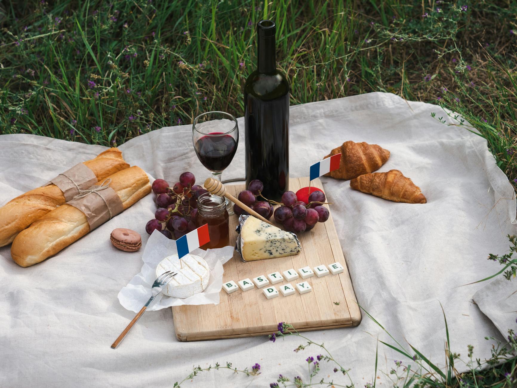 French picnic setup with baguettes, cheese, wine, and French flags celebrating Bastille Day outdoors.