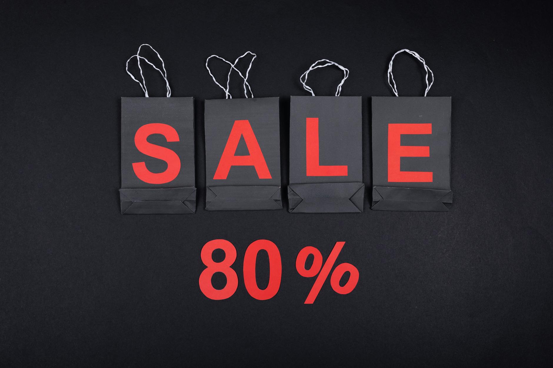 Highlighting a sale with 80% discount using black shopping bags and bold red text.