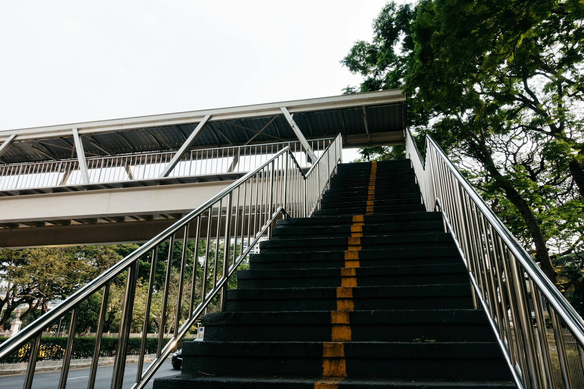 Entrecampos: o guia rápido para perceber o que está a ser construído 5 Image of a pedestrian overpass featuring stairs with metal railings and a yellow line, surrounded by greenery.
