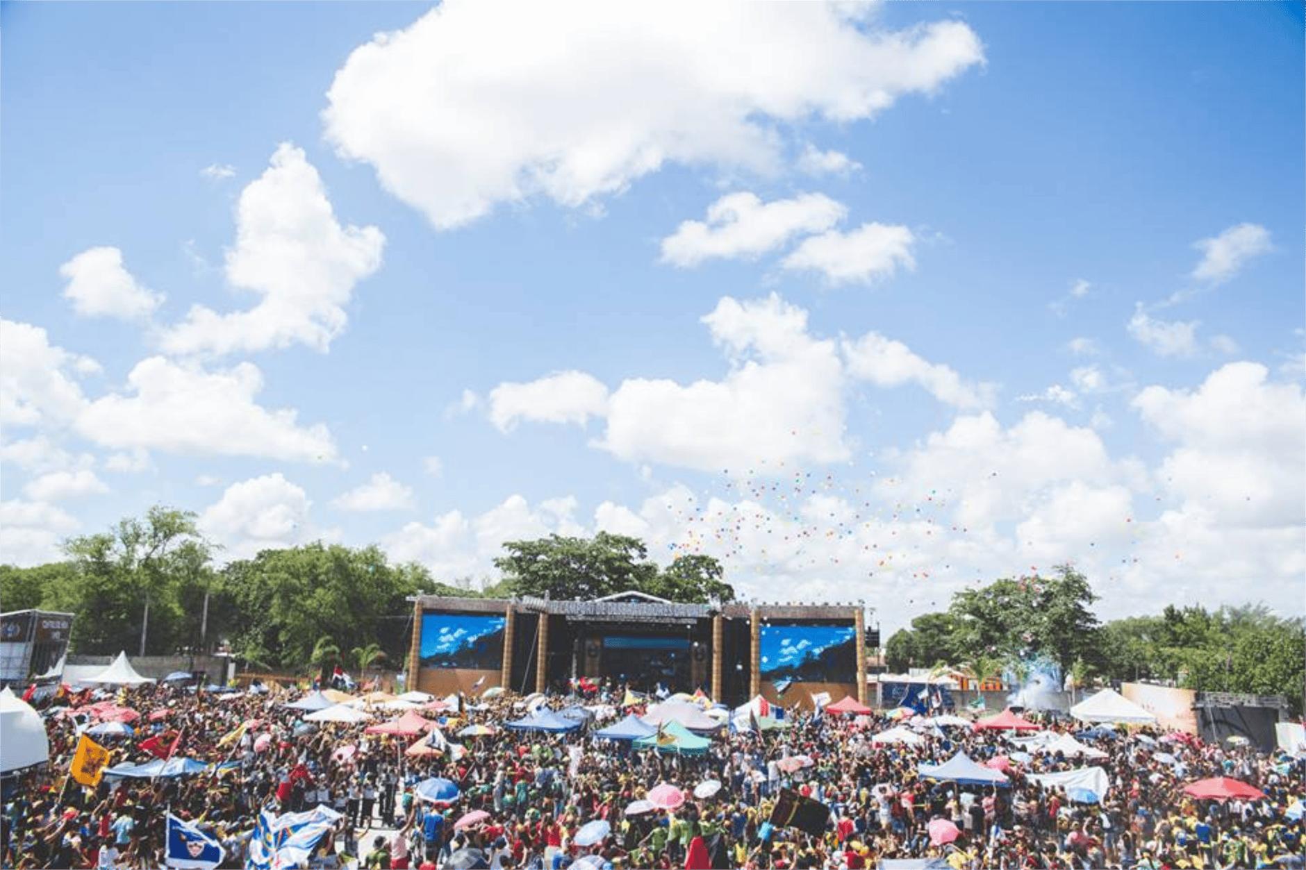 Festival dos Oceanos: concertos e atividades grátis — como descobrir as melhores 5 Lively outdoor festival with large crowd, vibrant umbrellas, and a clear sky in Santos Reis, Brazil.