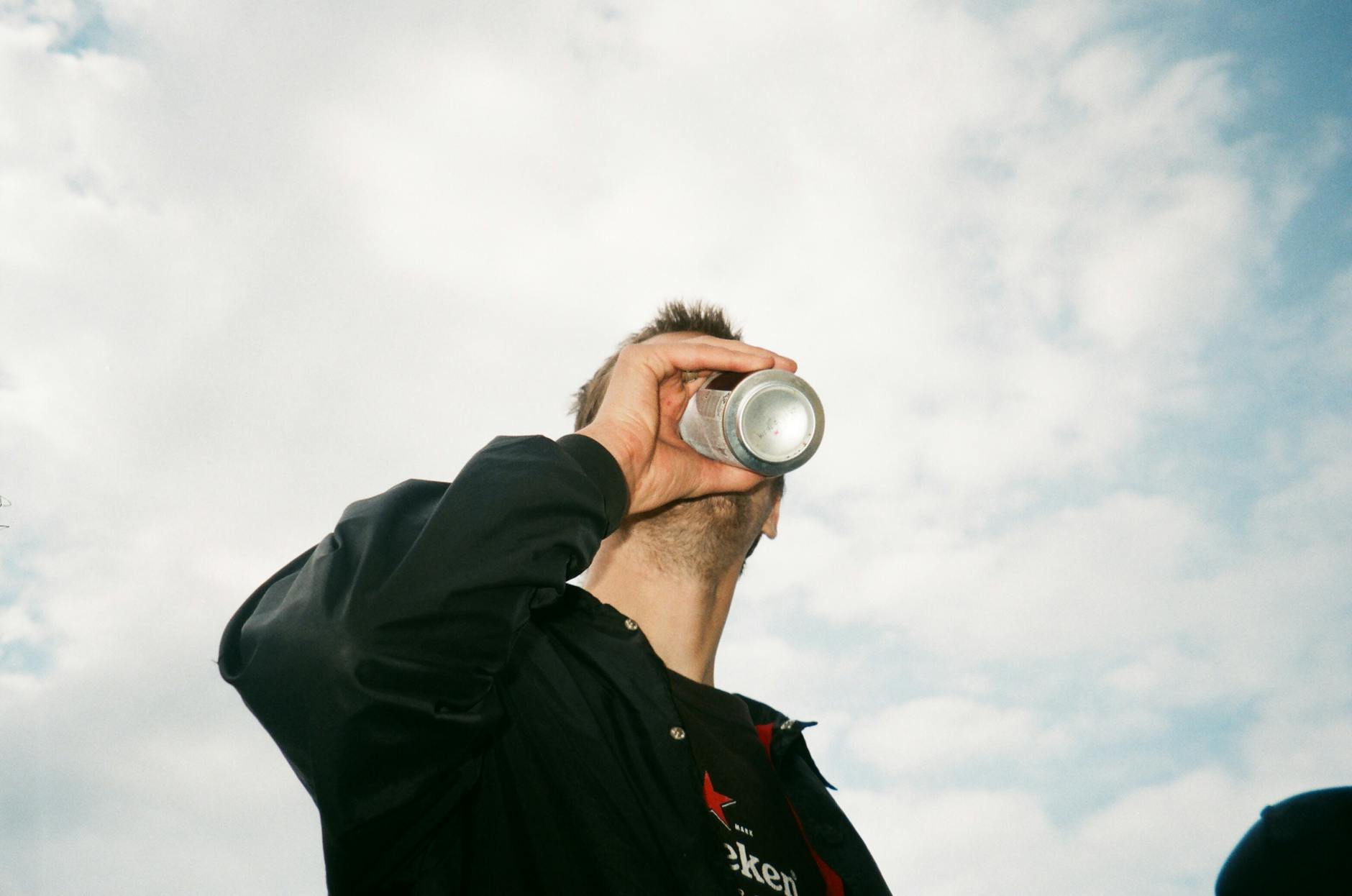 Low angle view of a man drinking from a can against a blue sky with clouds.