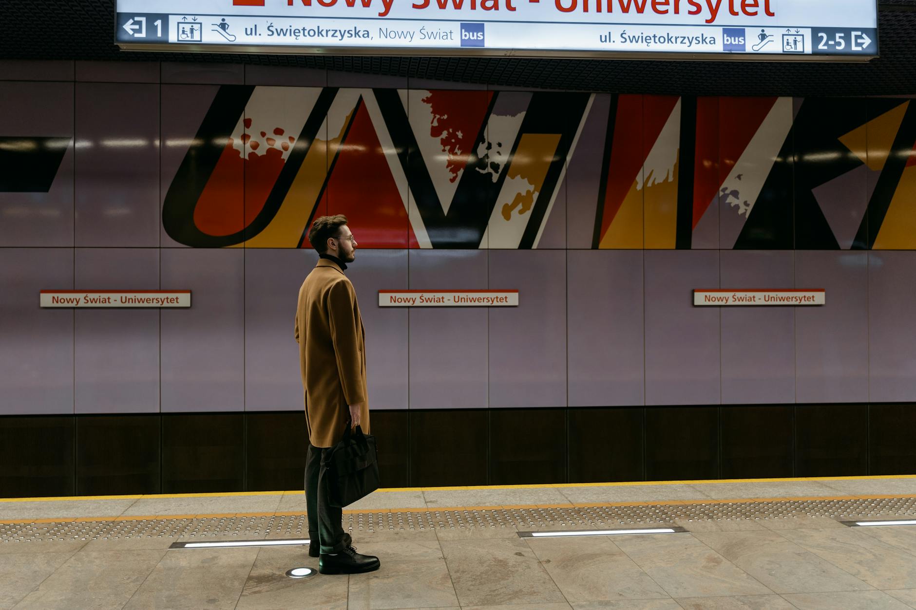 Man stands waiting on a colorful subway platform, showcasing urban commute.