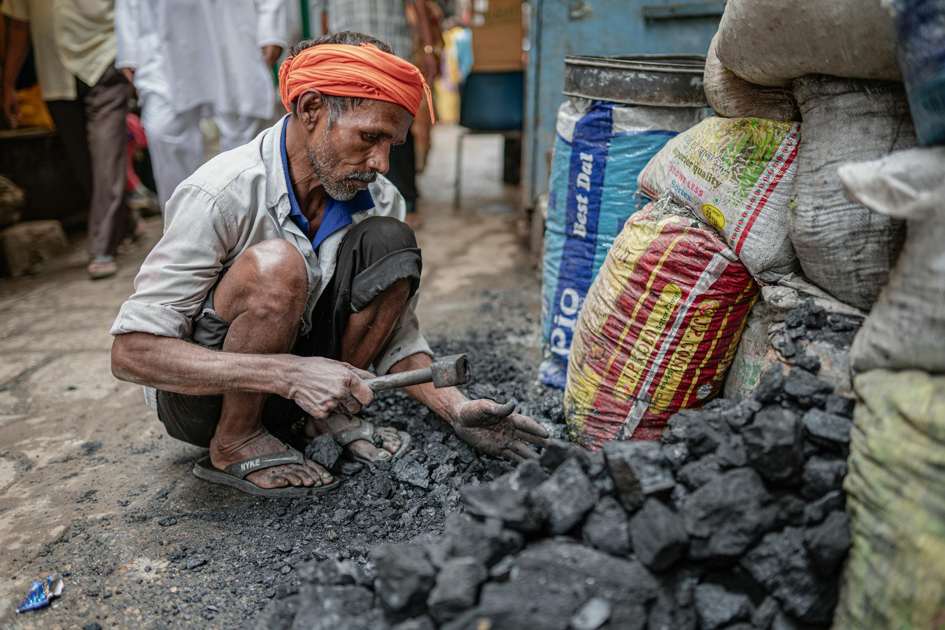 Mature man wearing turban sorts coal in an outdoor street market setting.