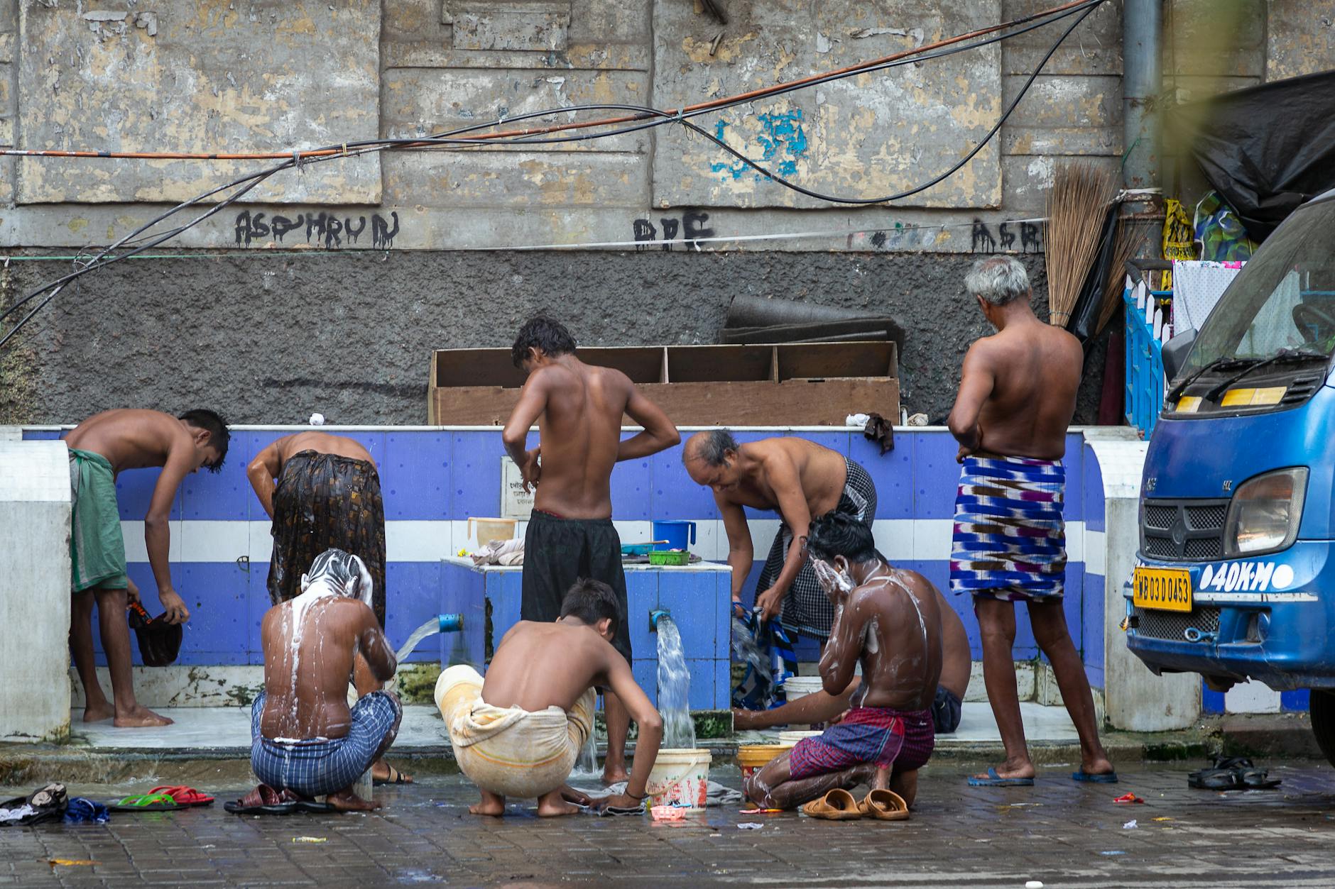 Spas E Banhos Em Lisboa: Onde Relaxar Sem Pagar Luxo 4 Men bathing outdoors, washing at a communal area in a city setting.