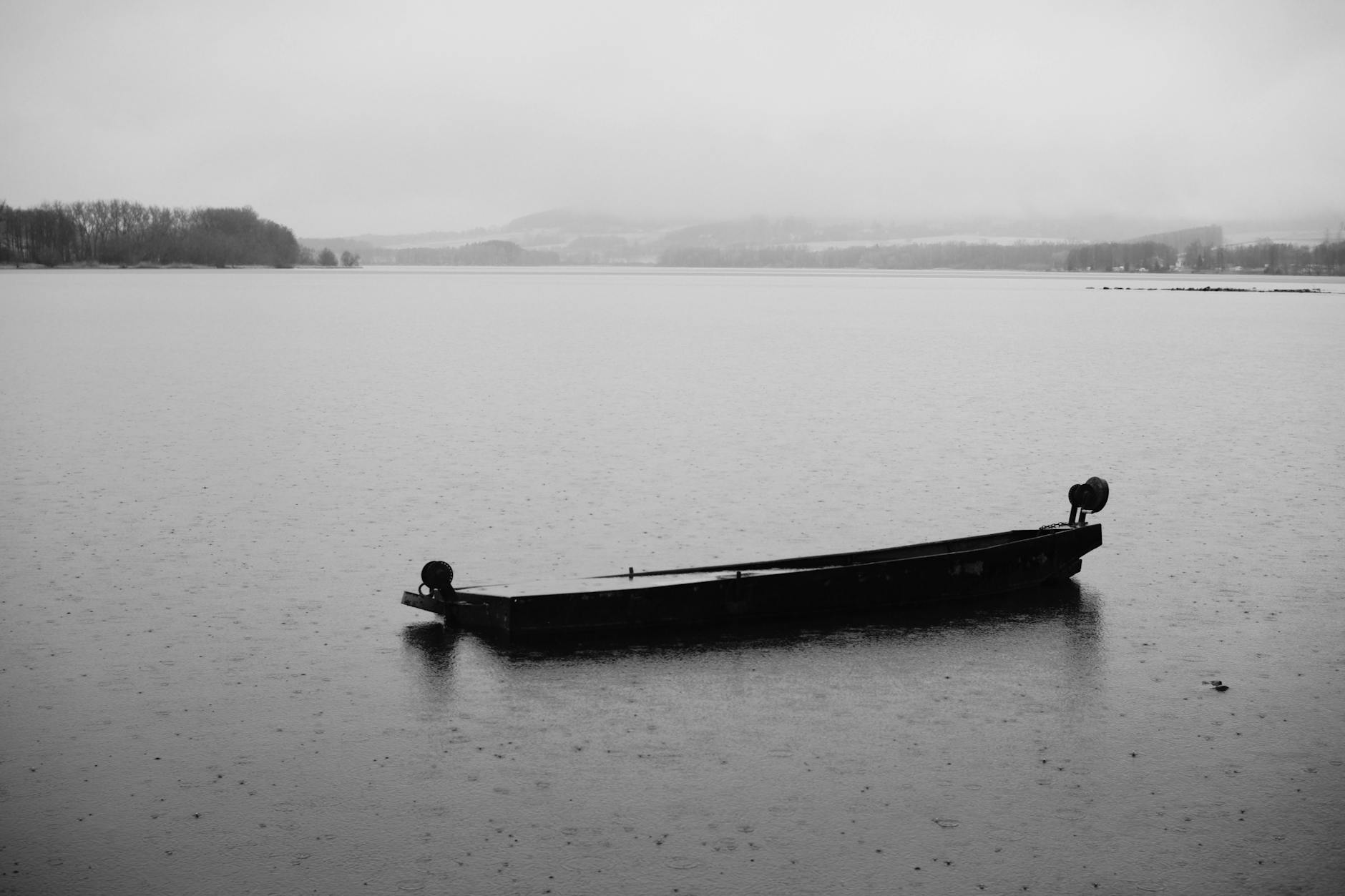 Miradouros para ir sozinho: onde te sentes bem sem “clima estranho” 2 Monochrome image of a lone boat floating on a tranquil lake, evoking solitude.