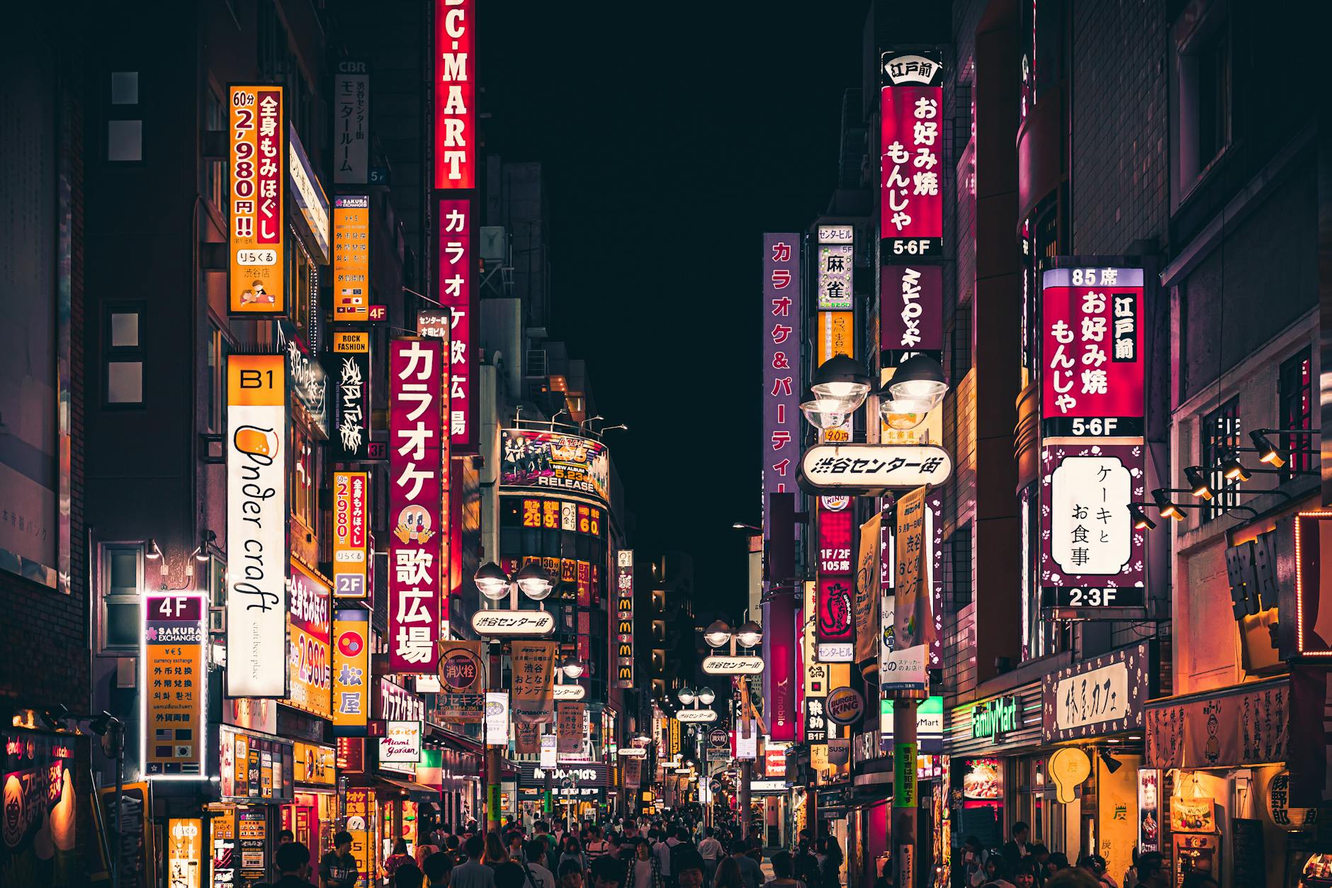 Night view of a busy Tokyo street with vibrant neon signs and people walking in Shinjuku, Japan.