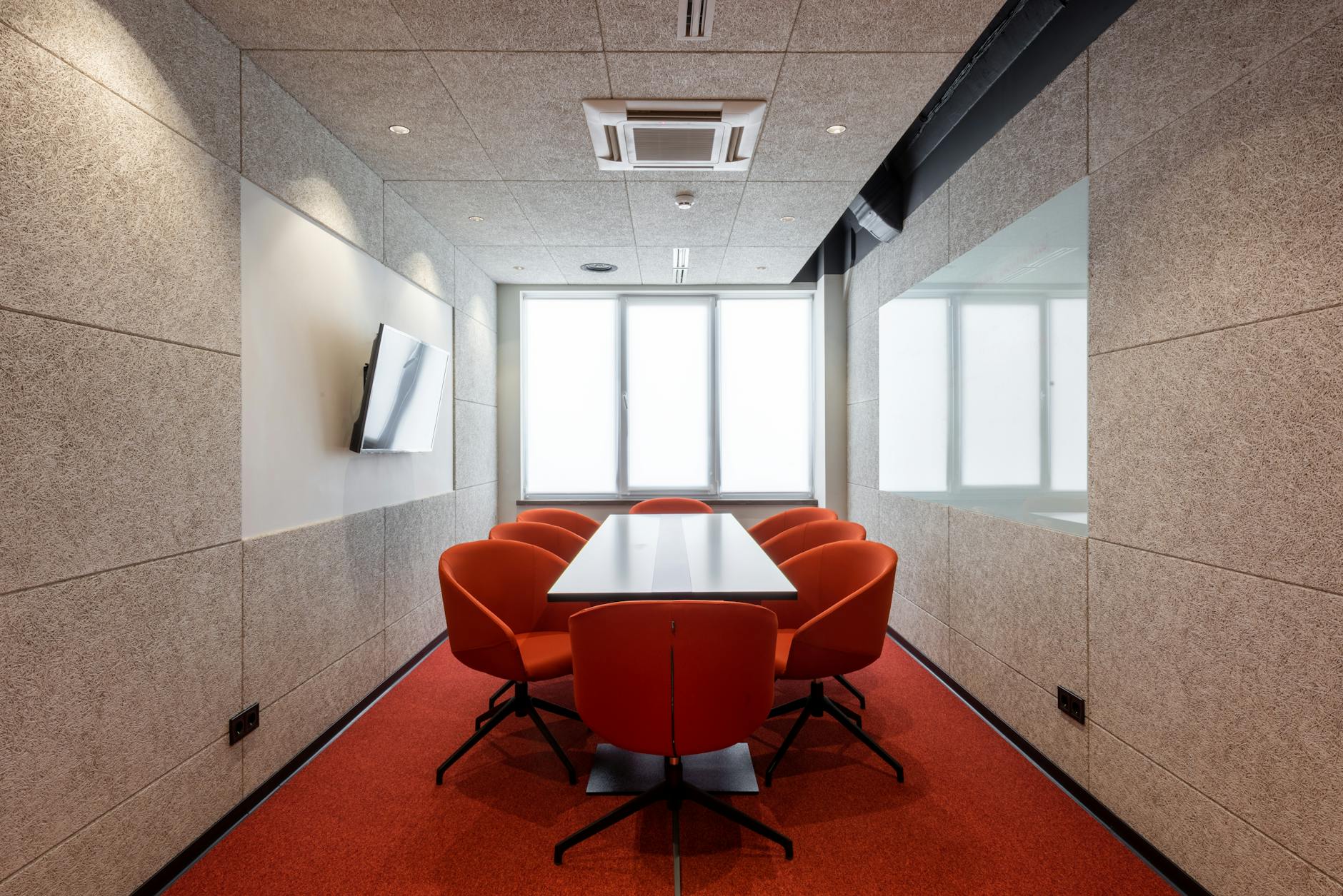 Parque das Nações: oportunidades de negócio que aparecem com mais escritórios 6 Orange chairs placed around white table in modern conference room with window and TV on wall in contemporary business center