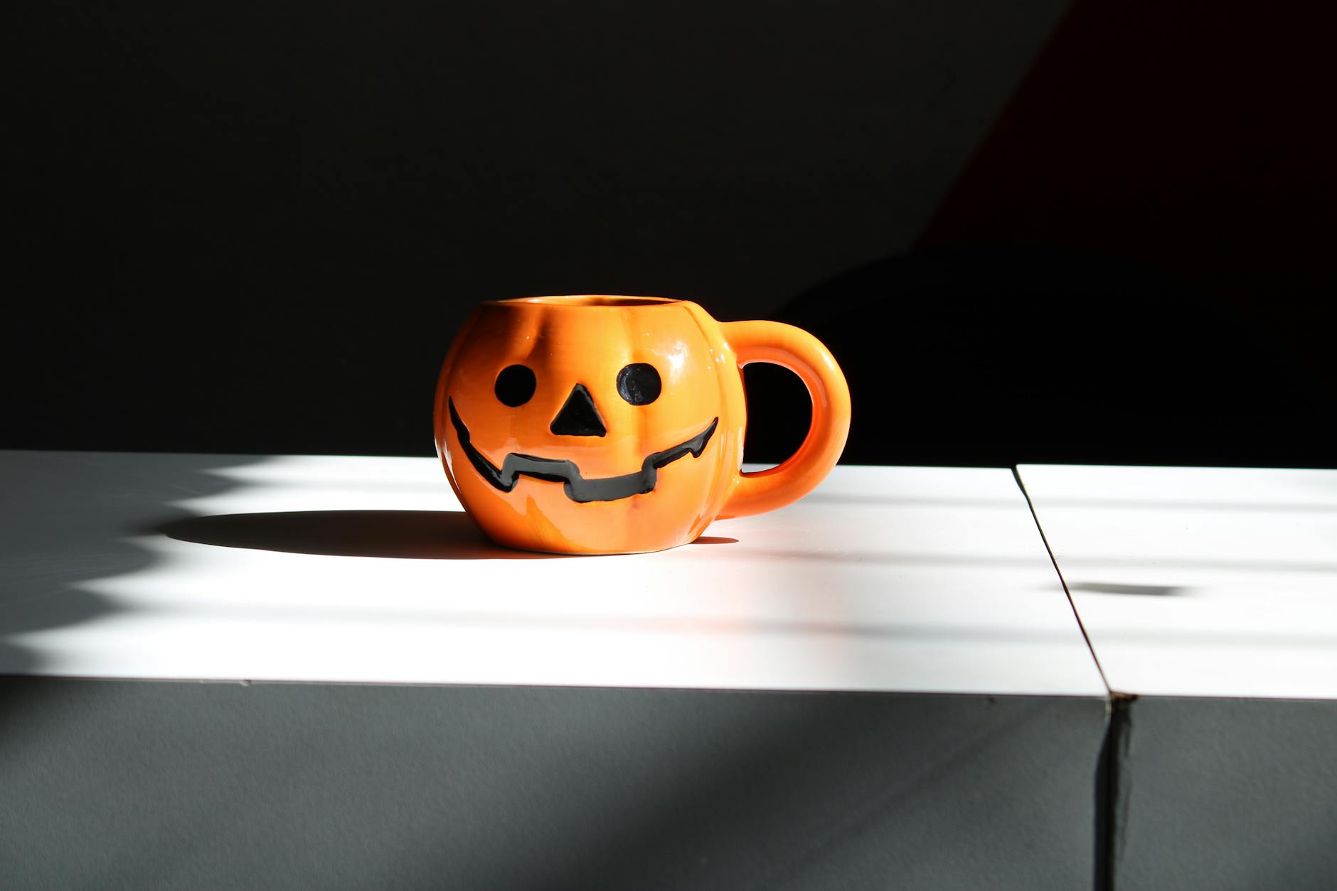 Orange pumpkin mug with jack-o'-lantern design on a white surface, capturing cozy fall vibes.