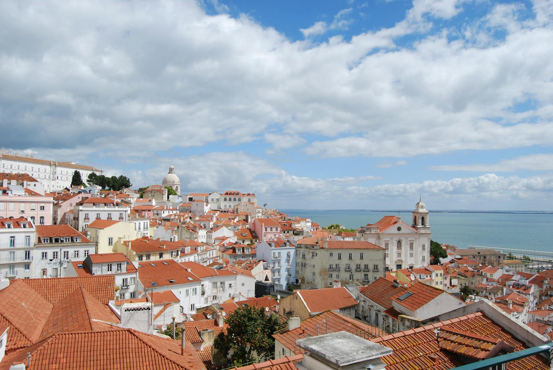 Panoramic view of Lisbon's Alfama district with traditional red roofs and the sea in the background.