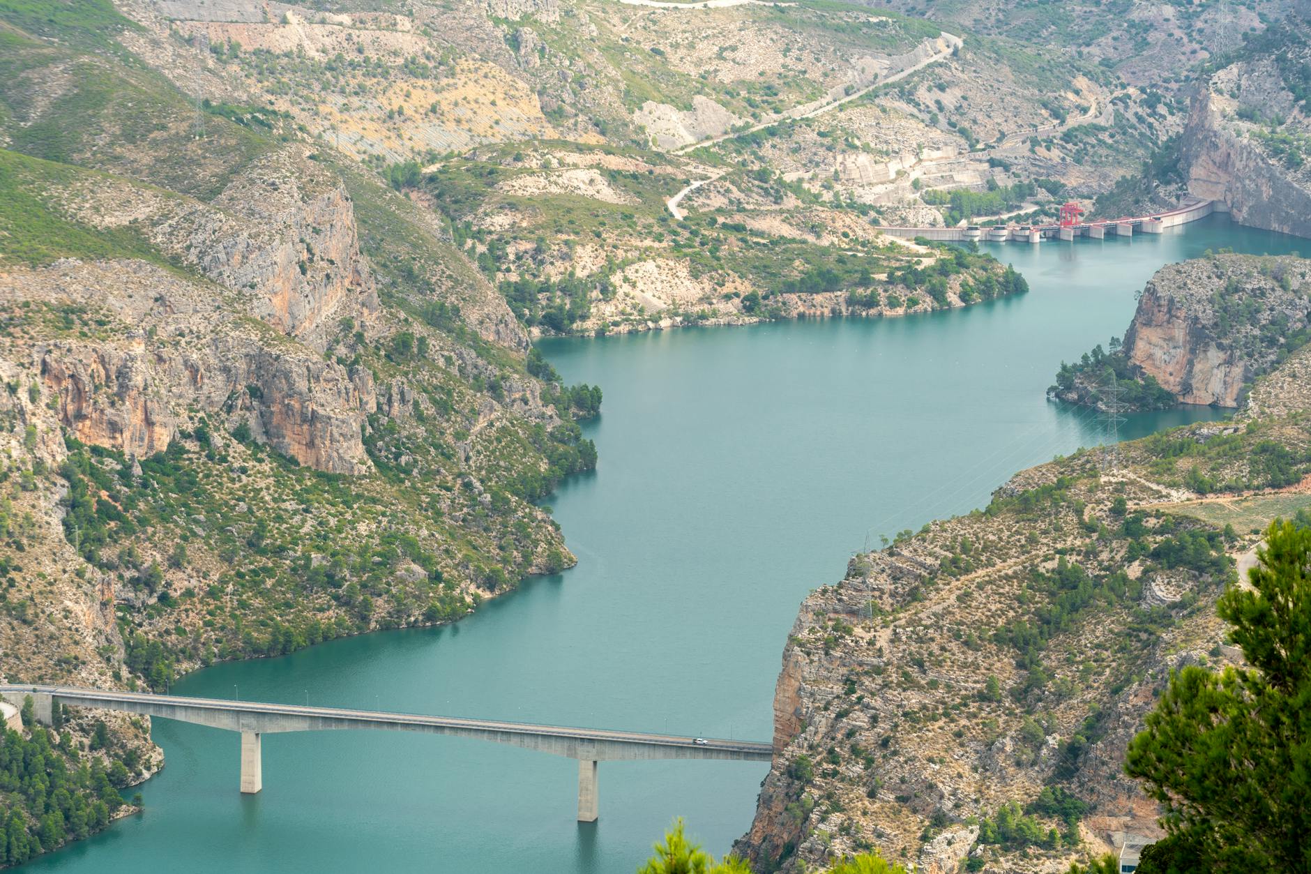 Lisboa 2026: como evitar ficar refém de desvios e cortes de trânsito 6 Panoramic view of turquoise waters and rocky cliffs in Cortes de Pallás, Spain, featuring a bridge and dam.