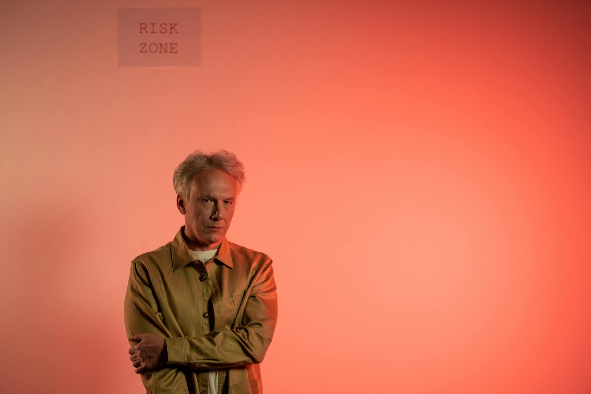 Portrait of a senior man standing indoors with a 'risk zone' warning and red background.