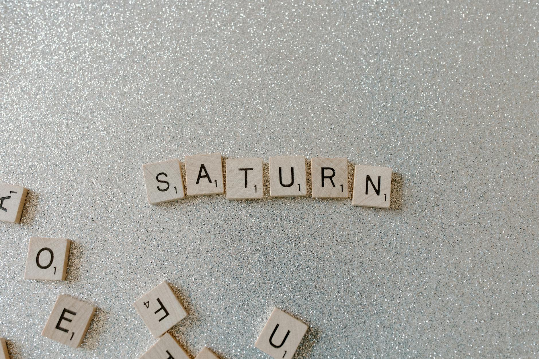 Scrabble tiles forming the word SATURN on a sparkling glitter background, space theme.