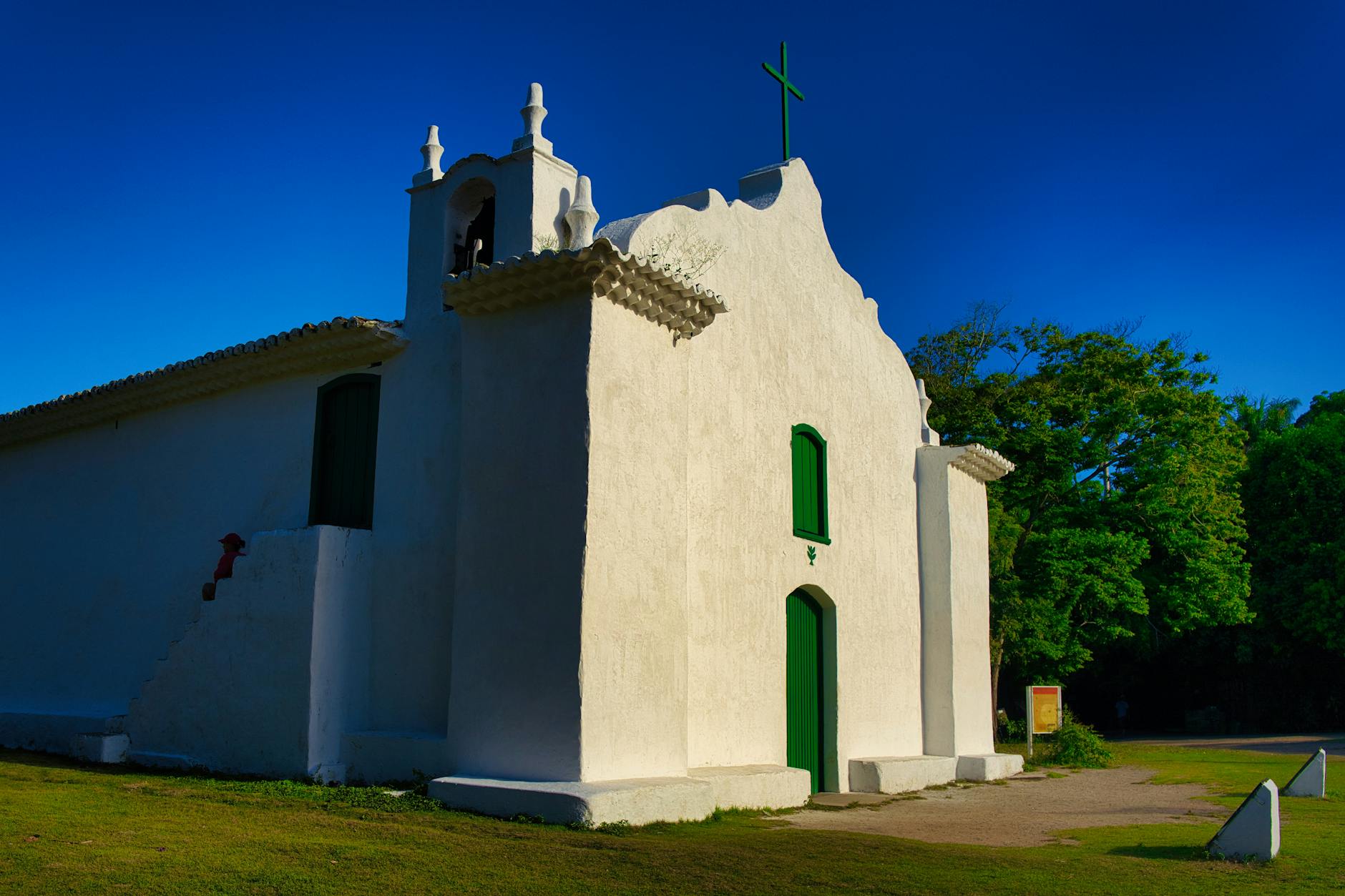 Sunlit historic church with white facade and green doors in Arraial d'Ajuda, Brazil.