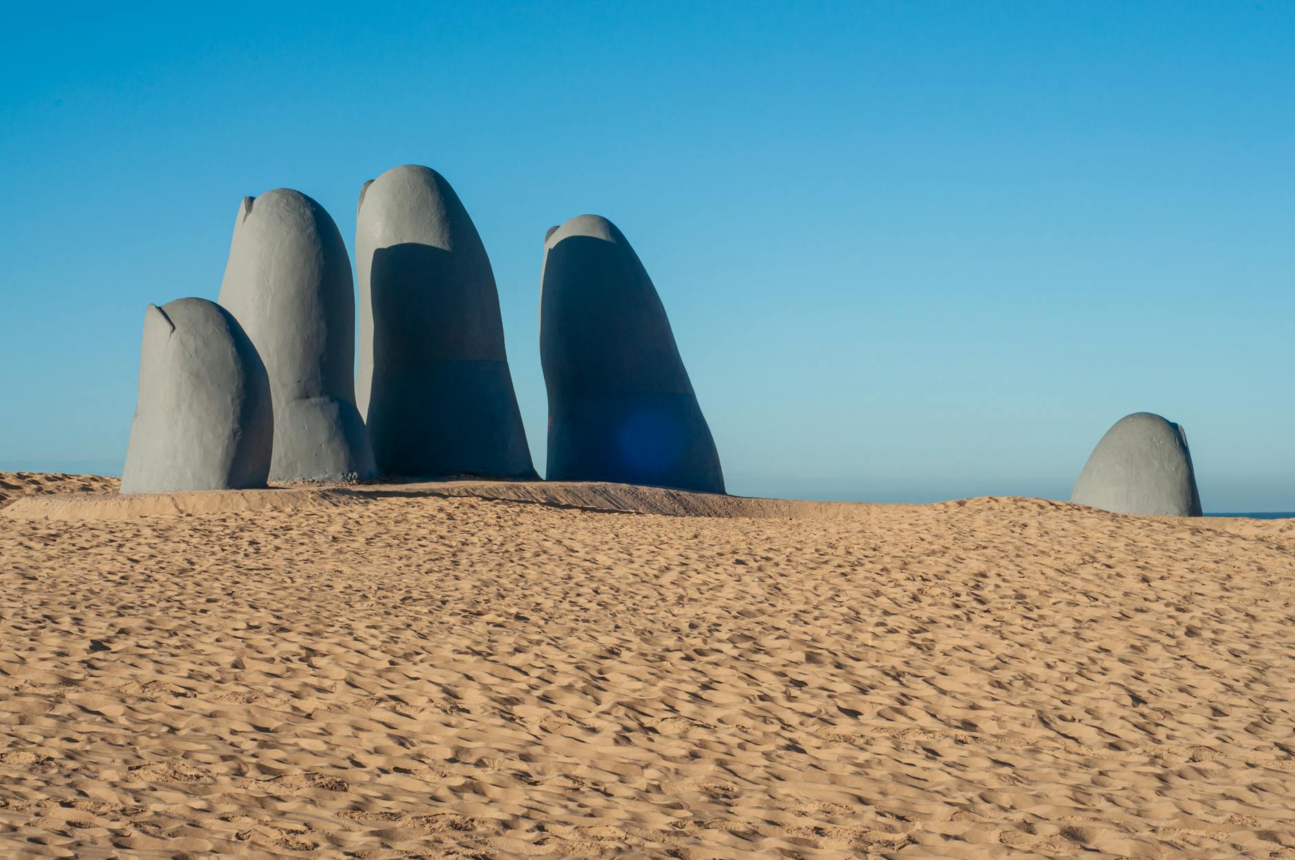 The Hand of Punta del Este sculpture emerges from the sand under a clear blue sky.