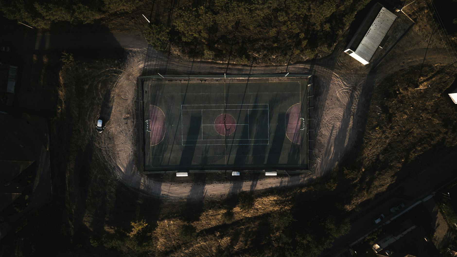 Top-down aerial view of an outdoor sports court surrounded by trees and lit path. Perfect for usage in sports or urban planning themes.