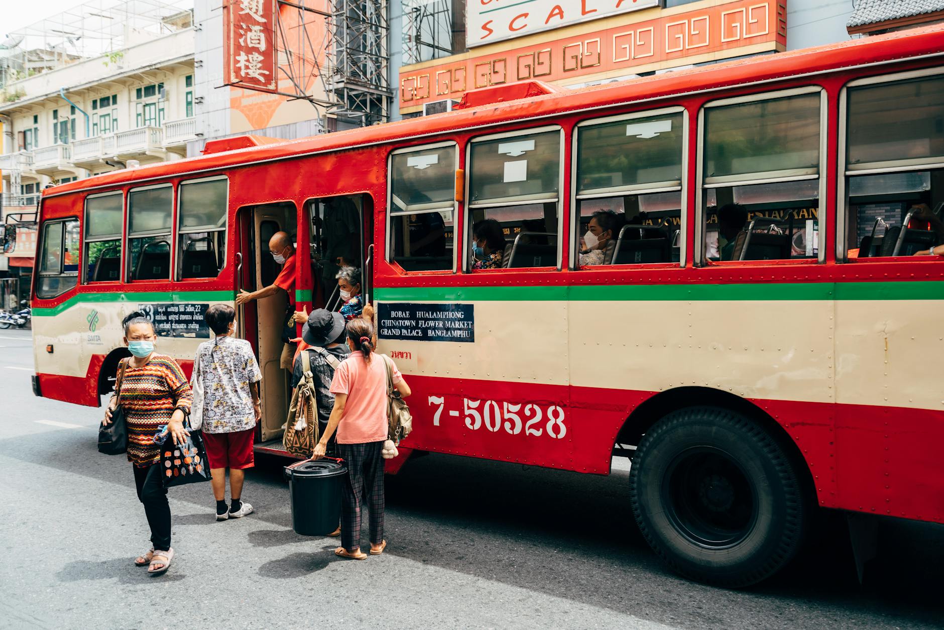 Vibrant city scene with people boarding a bus in bustling Bangkok, Thailand.