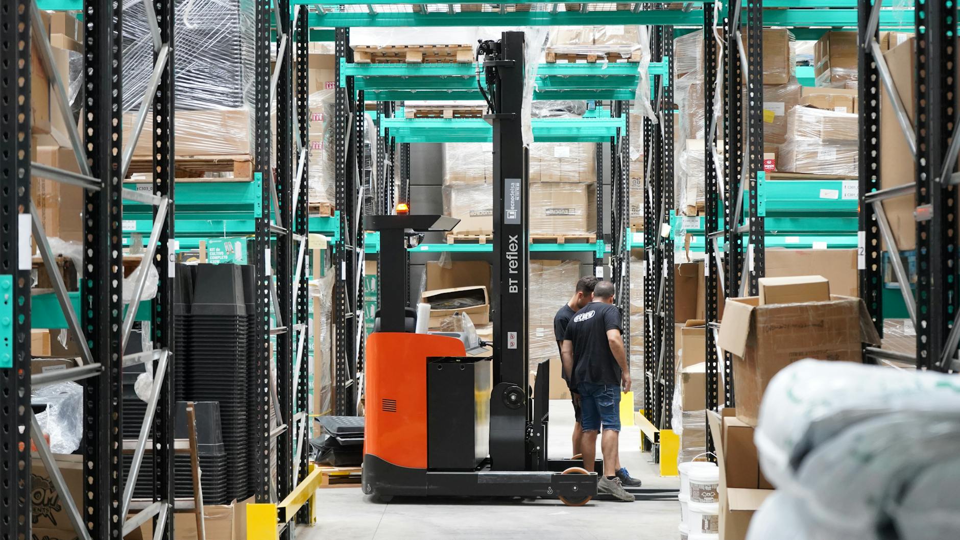 Parque das Nações: oportunidades de negócio que aparecem com mais escritórios 8 Warehouse scene featuring workers and a forklift navigating aisles for logistics and inventory management.