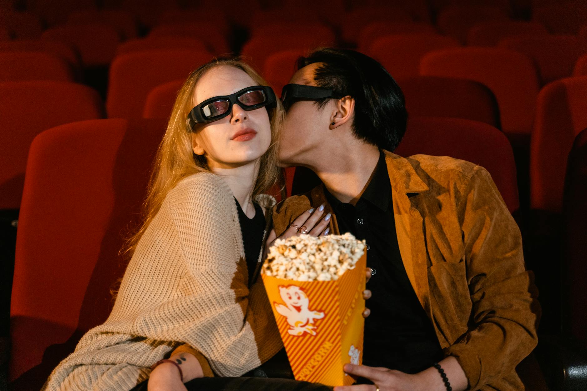Young couple enjoying a movie date with popcorn in a theater, wearing 3D glasses.